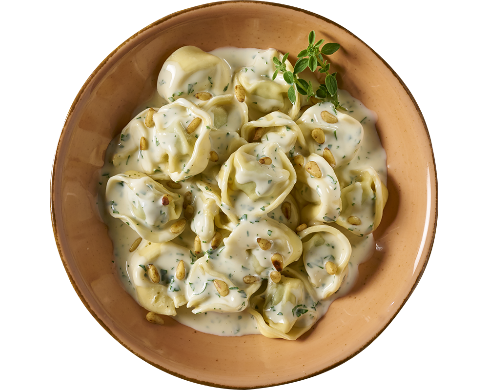 Eine Portion Tortelloni alla panna von Hofmanns Shop, gefüllt mit Ricotta und Spinat in einer cremigen Kräuter-Sahnesoße, garniert mit Pinienkernen und frischen Kräutern.