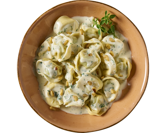 Eine Portion Tortelloni alla panna von Hofmanns Shop, gefüllt mit Ricotta und Spinat in einer cremigen Kräuter-Sahnesoße, garniert mit Pinienkernen und frischen Kräutern.