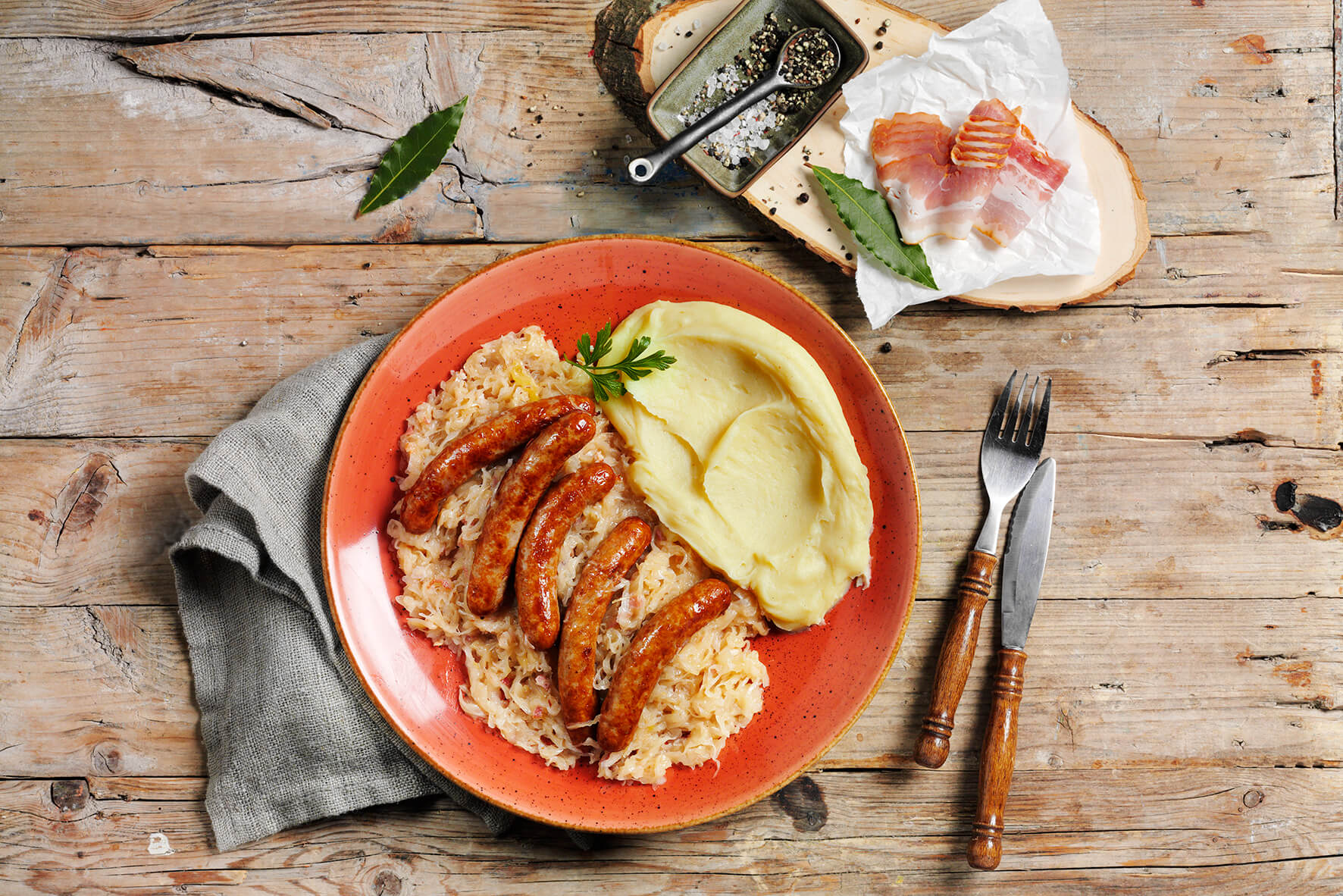 Hofmanns Glutenfreie-Box liefert wahre Genussmomente in Restaurantqualität mit einem Teller Würstchen, Sauerkraut und Kartoffelpüree, alles perfekt gewürzt und in rustikalem Ambiente mit Besteck serviert.