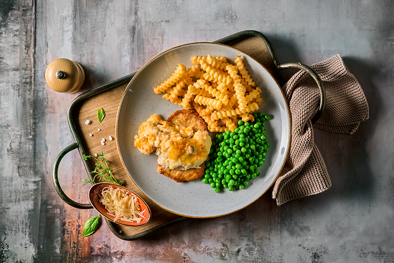 Ein Tablett mit Schweinesteak „au four“, Wellpommes und grünen Erbsen von HOFMANNs.