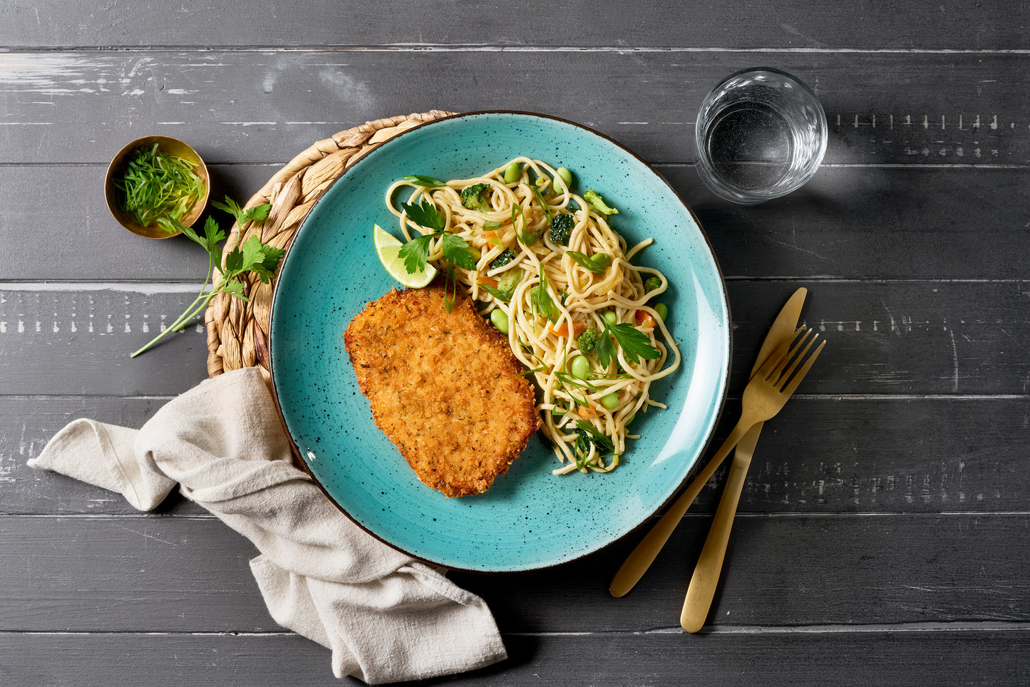 Schnitzel in Panko-Kräuter-Panade von Hofmanns Shop mit Gemüse-Nudeln auf blauem Teller.