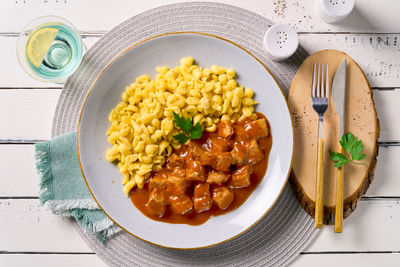 Ein Teller mit gepflanzten Steakhäppchen "Gulasch Style" von Hofmanns Shop mit Eierspätzle und Petersilie.