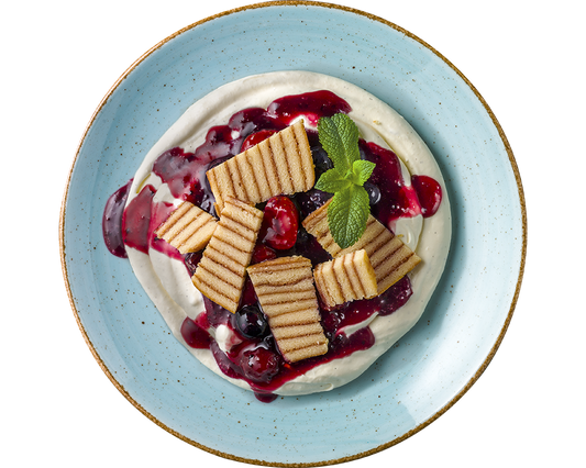 Dessert bestehend aus Baumkuchenstücken auf Mascarpone-Creme, ergänzt durch Beerensauce, Schichtwaffeln und garniert mit Minze auf einem blauen Teller von Hofmanns Shop.