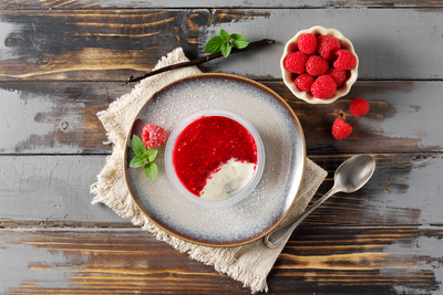 Bayrische Creme mit Himbeere von Hofmanns Shop, mit Sahne und Minze, serviert auf rustikalem Tisch.