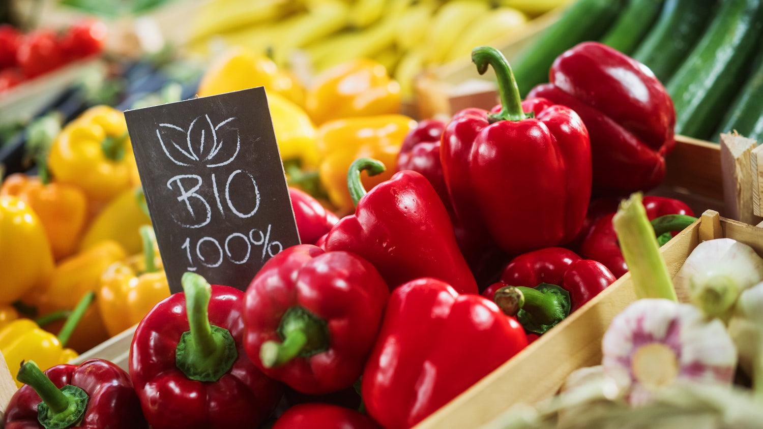 Nahaufnahme einer farbenfrohen Auslage auf einem Bauernmarkt mit Paprika und einem Schild mit der Aufschrift „BIO 100 %“.