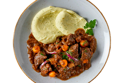 Ein Teller mit Boeuf à la Bourguignon von Hofmanns Shop, cremigem Kartoffelstampf, einem Eintopf aus zartem Rindfleisch mit Karotten und Zwiebeln, alles garniert mit Petersilie und liebevoll mit Rotwein geschmort für mehr Geschmackstiefe.