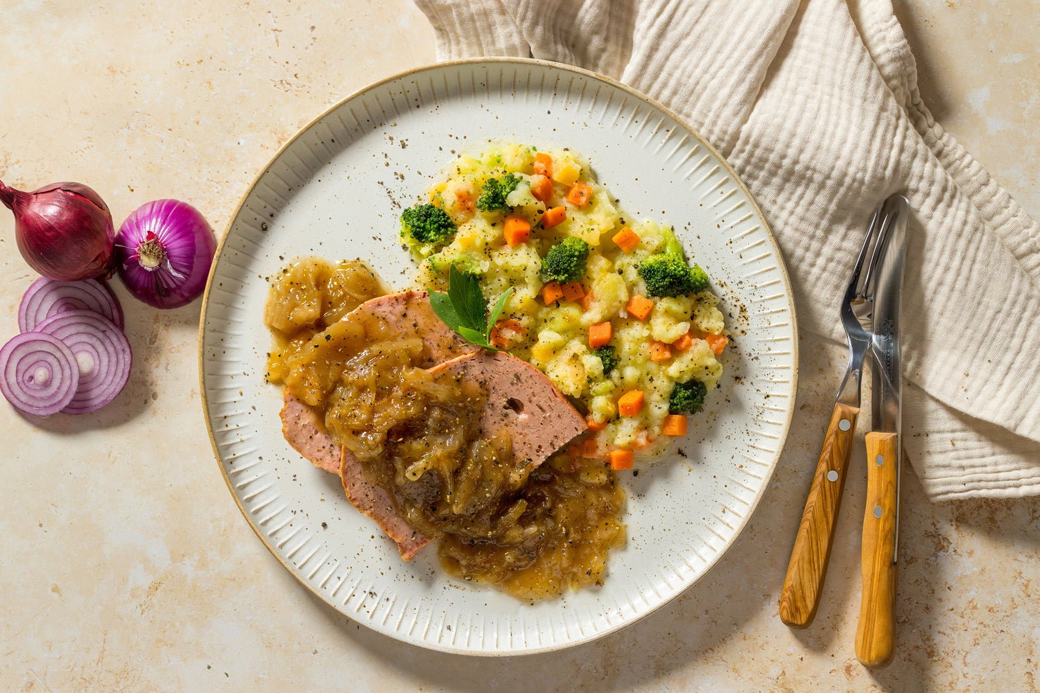 Teller mit Hackbraten, Zwiebelsoße und Kartoffelpüree mit Gemüse. Serviette und Besteck daneben.