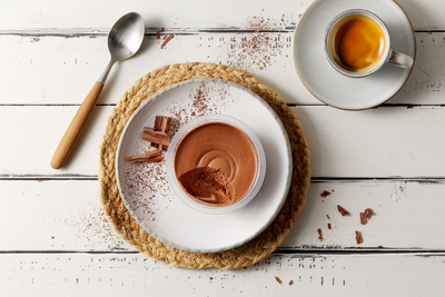 Eine Tasse Espresso und Mousse dunkel von Hofmanns Shop mit Schokoladenraspeln auf einem weißen Tisch.