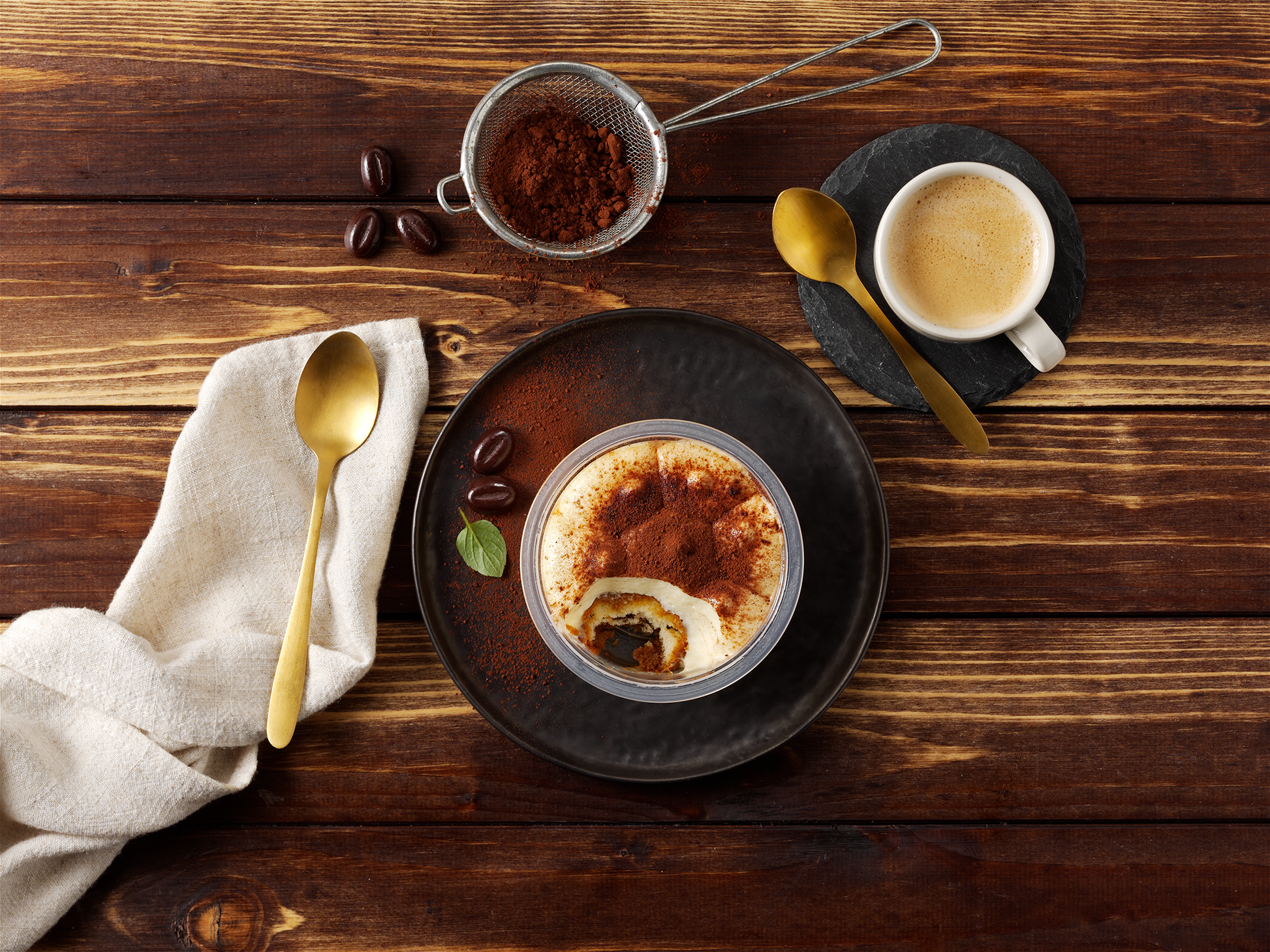 Tiramisu Klassik von Hofmanns Shop: Biskuit & Mascarponecreme auf dunklem Teller mit Kaffee & Kakaopulver.