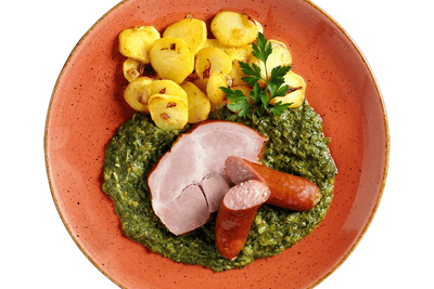 Ein Teller mit HOFMANNs Grünkohl „Norddeutsche Art“, Würstchen, Bratkartoffeln und cremigem Spinat.