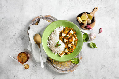 Eine verlockende Schüssel Reis-Paneer-Curry auf einem grünen Teller mit Löffel, Gewürzen und Zutaten daneben – ein echter Bestseller aus der Probierbox von Hofmanns Shop: Fleischfreie Alternativen.