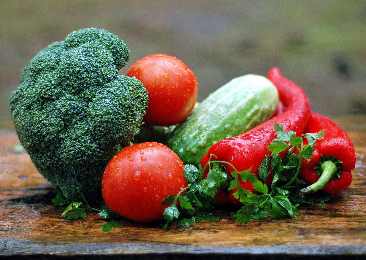 Eine Nahaufnahme von frischem Gemüse: Brokkoli, Tomaten, Gurken, rote Paprika und Petersilie auf einer Holzoberfläche.