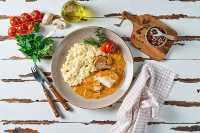 Ein Teller Filetteller von Hofmanns Shop mit Kartoffelpüree und Bratensoße, garniert mit Kräutern, auf einem rustikalen weißen Holztisch.