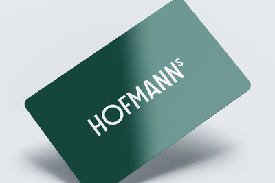 Grüne Geschenkkarten mit der Aufschrift „HOFMANNs“ in weißer Schrift auf einer geneigten, schattigen Oberfläche.
