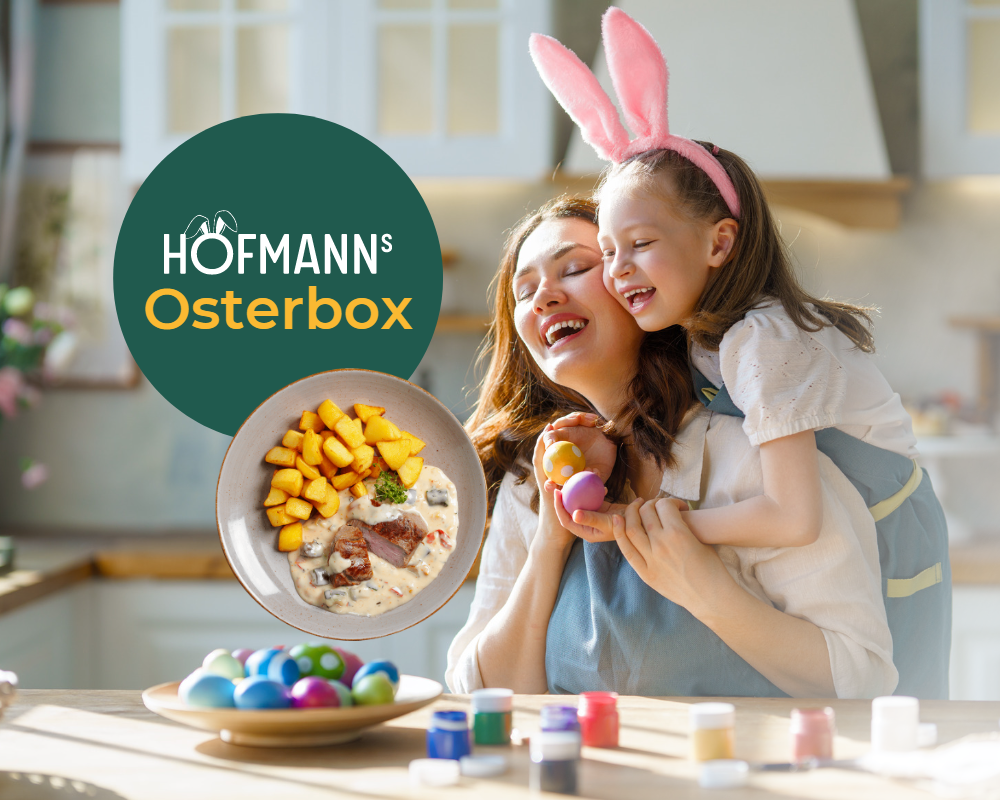 Eine Frau und ein Kind mit Hasenohren lächeln in einer Küche mit der HOFMANNs Osterbox von Hofmanns Shop, gefüllt mit festlichem Geschirr und dekorierten Eiern.