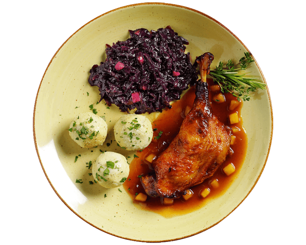 Ein Teller mit Hofmanns Entenkeule, serviert mit Knödeln, Apfelrotkohl und Rosmaringarnitur, begleitet von einer würzigen Bratapfelsoße.