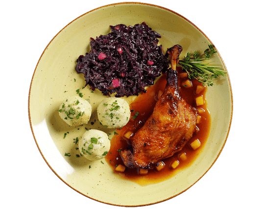 Ein Teller mit Hofmanns Entenkeule, serviert mit Knödeln, Apfelrotkohl und Rosmaringarnitur, begleitet von einer würzigen Bratapfelsoße.